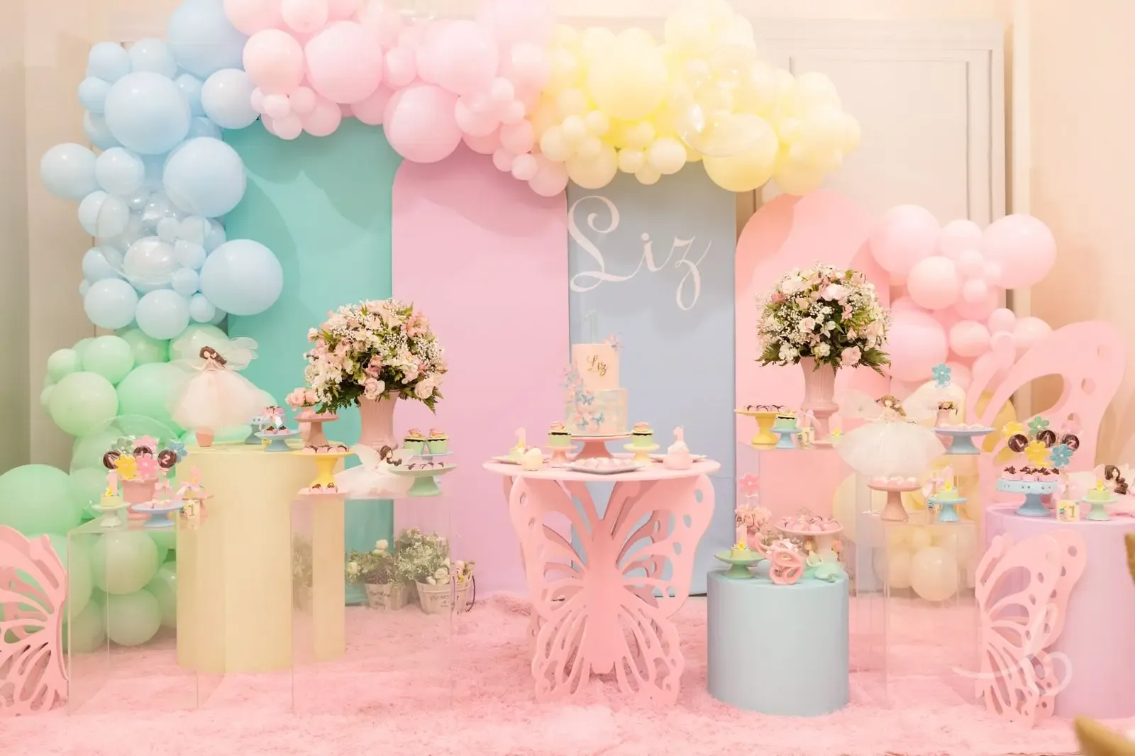 Decoração de festa em cores pastel, com balões e cenário personalizado
